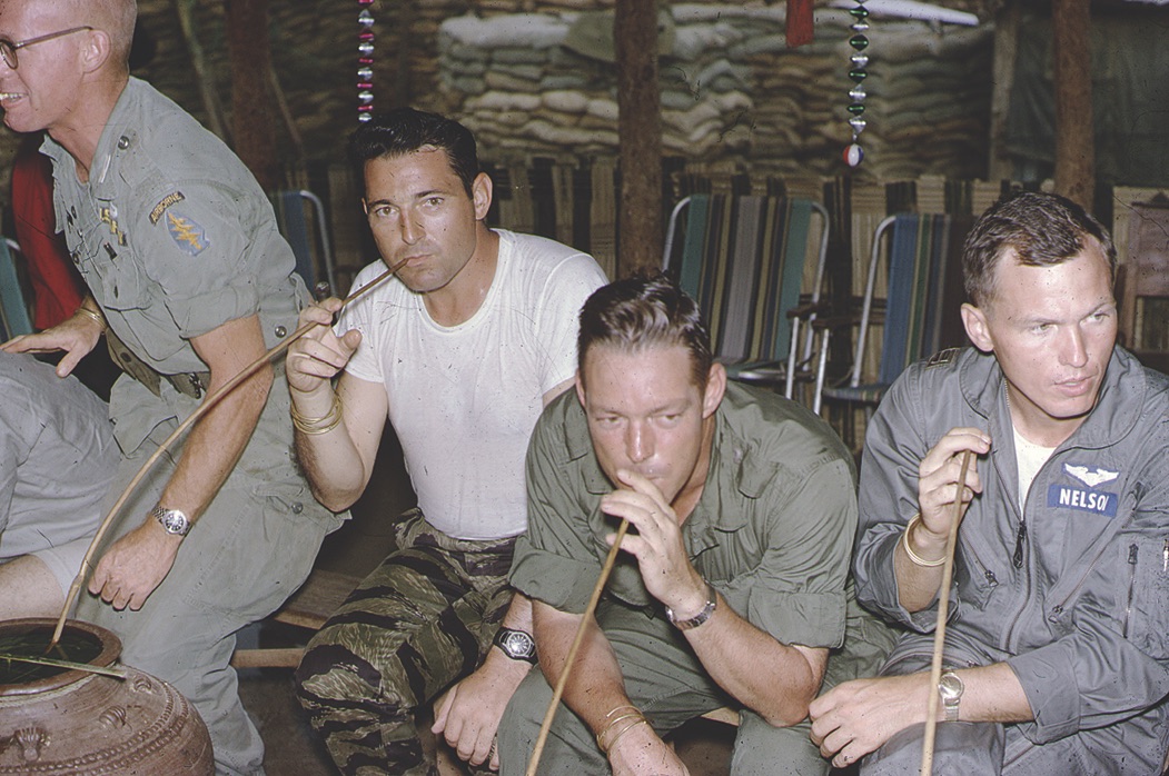 American servicemen in the Highlands imbibe Numpai, a potent Montagnard rice wine central to tribal life. / Richard "Dick" Shortridge