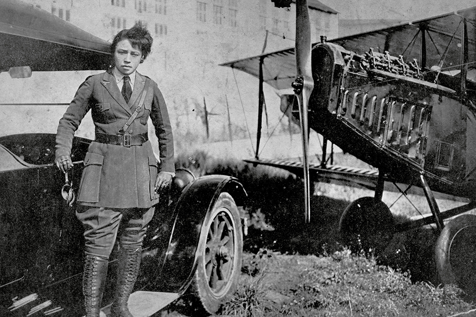 Coleman in her tailor-made uniform standing on the running board of a Ford Model T with her Curtiss JN-4 Jenny. (NASM 93-16054)
